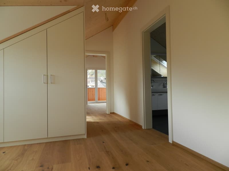 Empty hallway with wooden flooring, white walls, built-in closet, and an open doorway leading to another room.