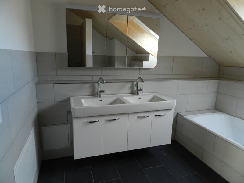 Modern bathroom with a double sink, sleek white cabinetry, and a large mirror above the sink. The room features dark tiled flooring and a bathtub on the right side.