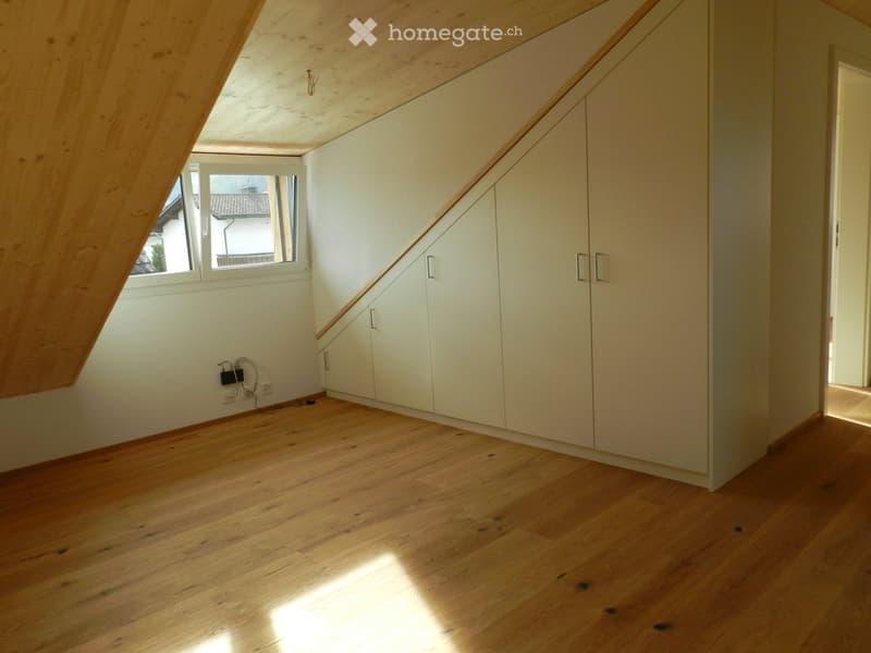 Empty attic room with wooden floor, white built-in wardrobes, and a small window letting in natural light.