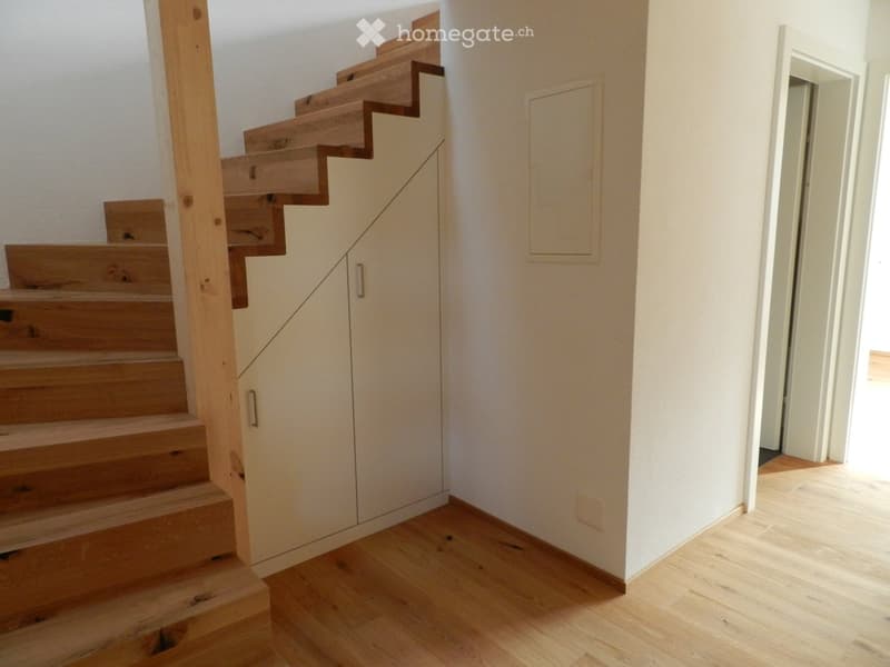 Wooden staircase with open risers and a built-in storage unit on one side, leading to an adjacent room with light-colored flooring.