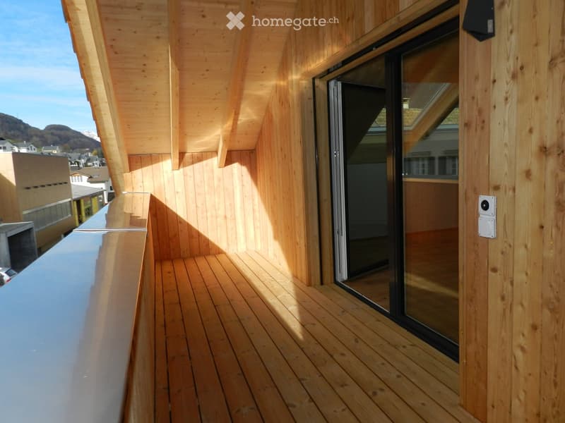 Wooden balcony with glass sliding doors, wooden decking, and a view of the surrounding area.