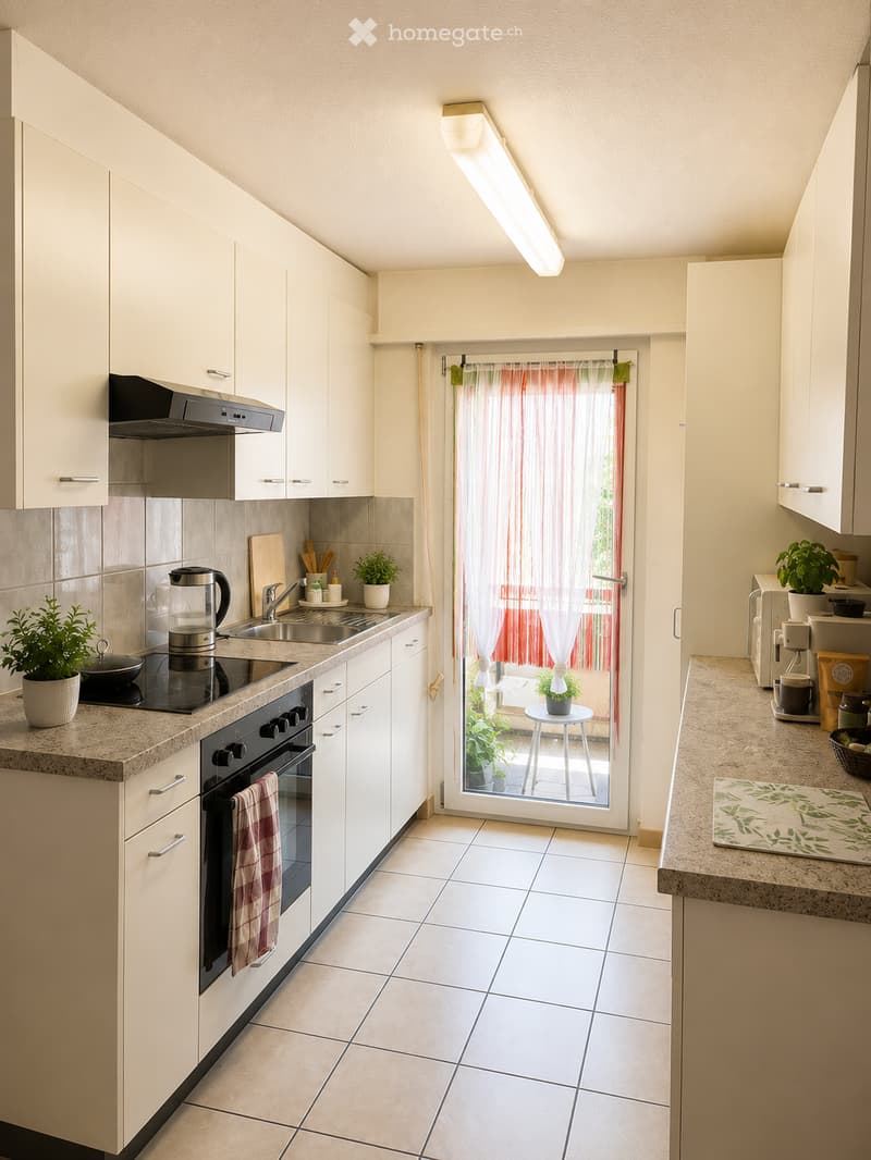 Modern kitchen with white cabinets, tiled floor, granite countertops, and stainless steel appliances. Features an oven, stove, sink, coffee maker, and a small table with a plant visible through the open door.