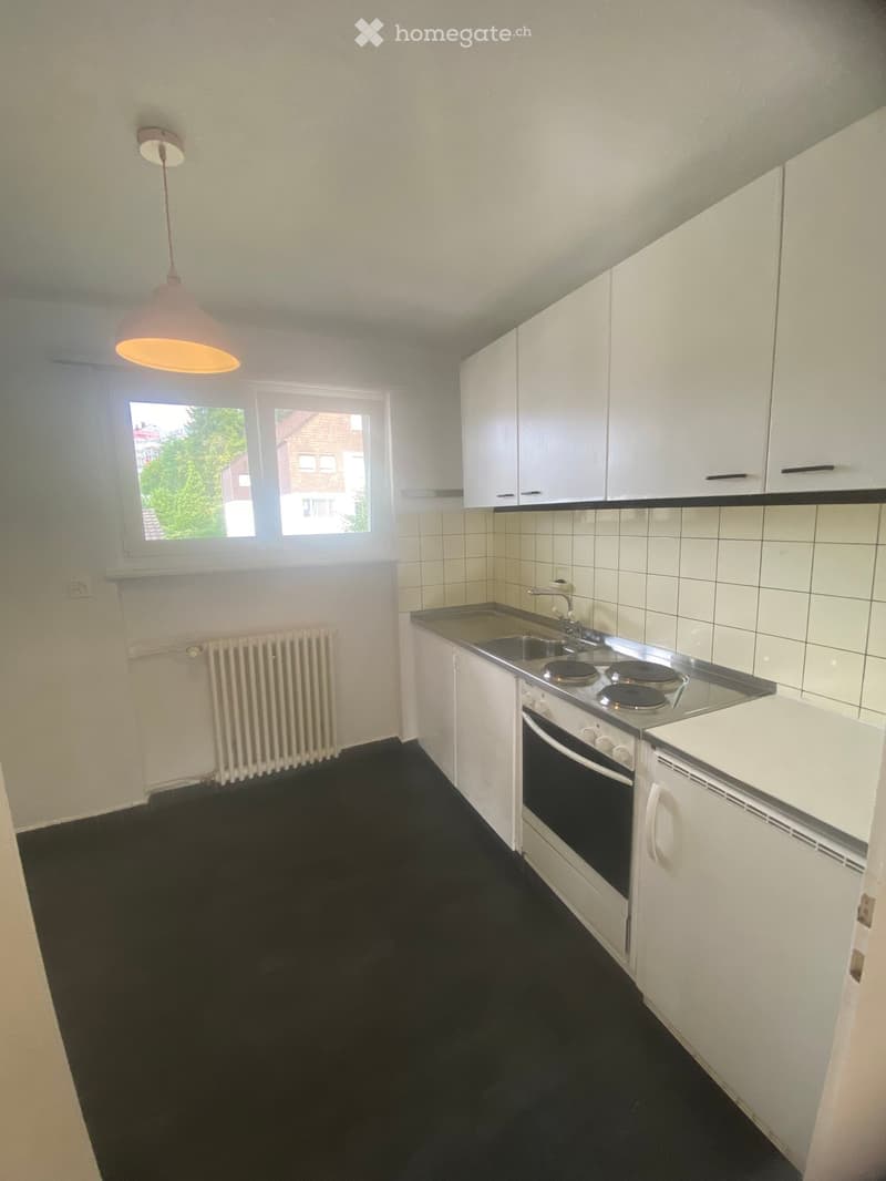 Modern kitchen with white cabinets, stainless steel sink, electric stove, and built-in oven. Features a black tiled backsplash, black floor, and a window with a view of greenery.