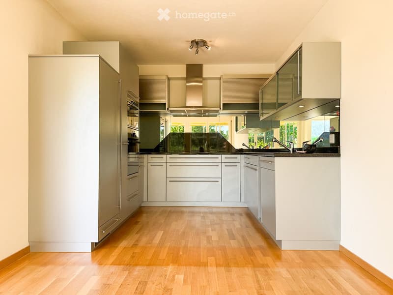 Modern kitchen with light-colored cabinets, wooden flooring, stainless steel appliances, and a central island with a sink and faucet.