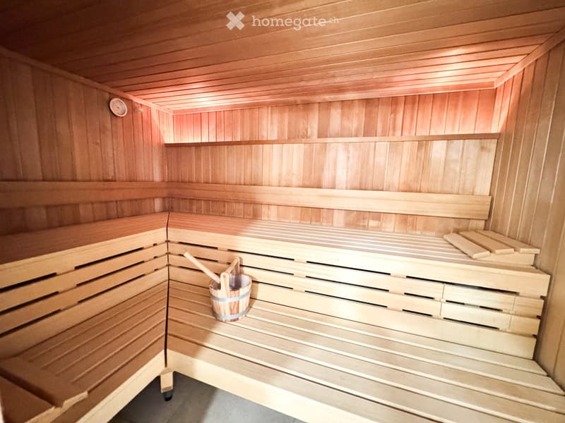Wooden sauna with benches, a small wooden bucket, and a wooden paddle placed on the floor.