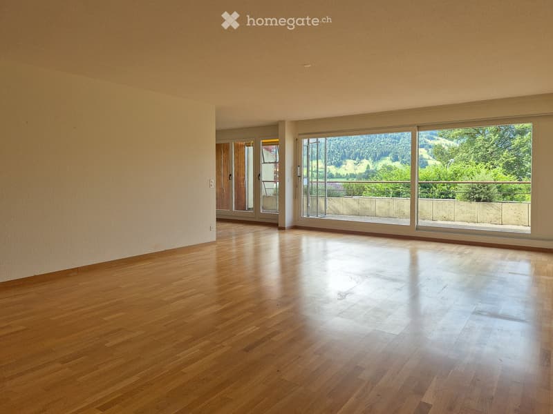Empty room with wooden flooring, large windows, and a scenic view of greenery outside.