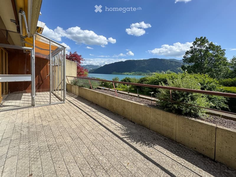 Balcony with a view of a lake and mountains, featuring a metal railing and a glass enclosure.