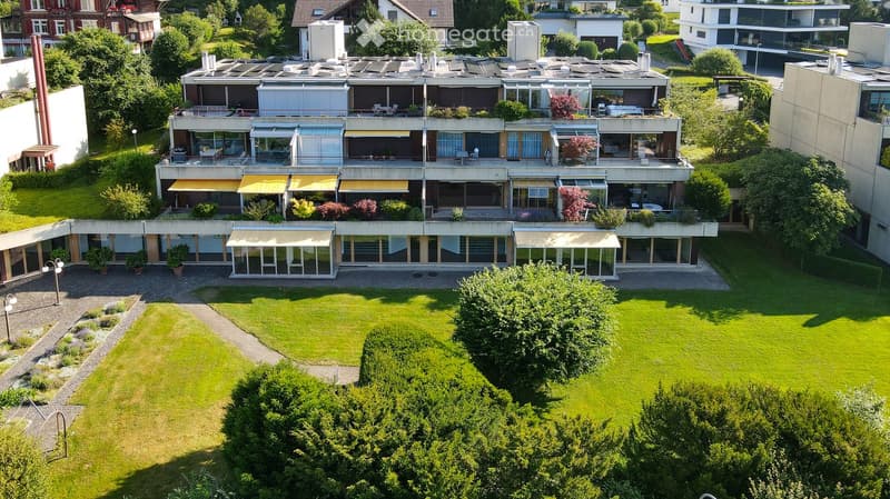 A modern multi-story residential building with large windows, balconies, and a well-maintained lawn in front.