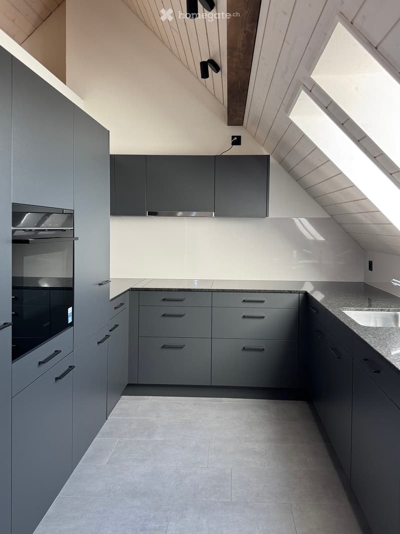 Modern kitchen with grey cabinets, granite countertop, and built-in oven. Features a sleek design with ample storage and a spacious layout.