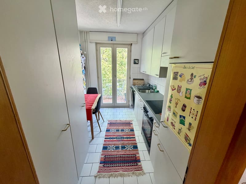 Modern kitchen with white cabinets, stainless steel appliances, a colorful runner rug, and a small dining area with a table and chairs.