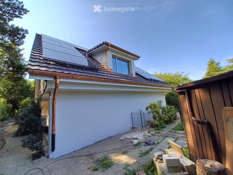 Two-story house with white walls, brown roof, solar panels, and a small gate.
