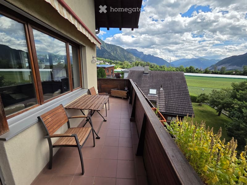 Balcony with wooden table and chairs, overlooking a scenic mountain view and countryside.