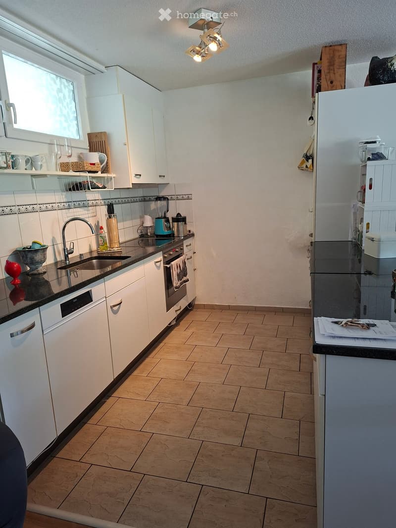 Modern kitchen with white cabinets, stainless steel appliances, and a tiled floor. Features include a refrigerator, oven, sink, faucet, and various kitchen items on the countertops.