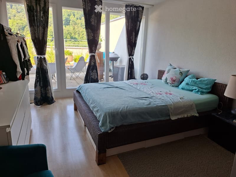 Bright bedroom with a large bed, nightstand, lamp, and a view of a balcony area with outdoor furniture.