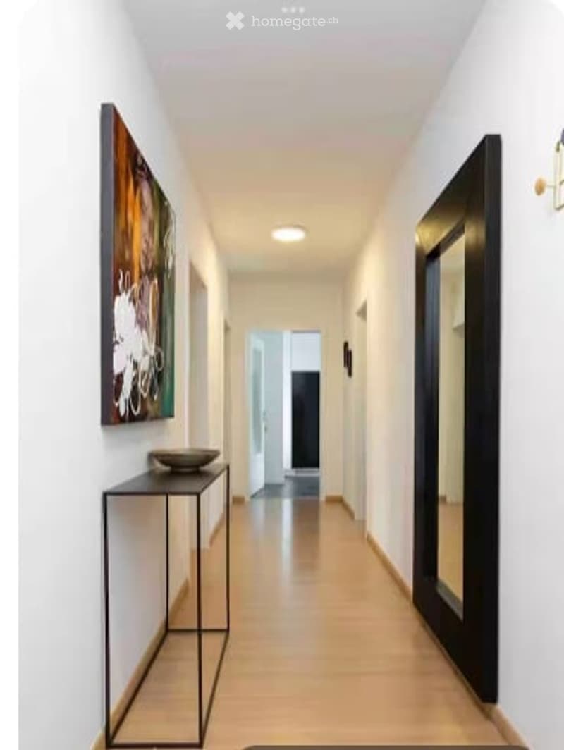 Modern hallway with white walls, wooden flooring, recessed lighting, a small black console table with a bowl, and a large abstract painting on one wall.