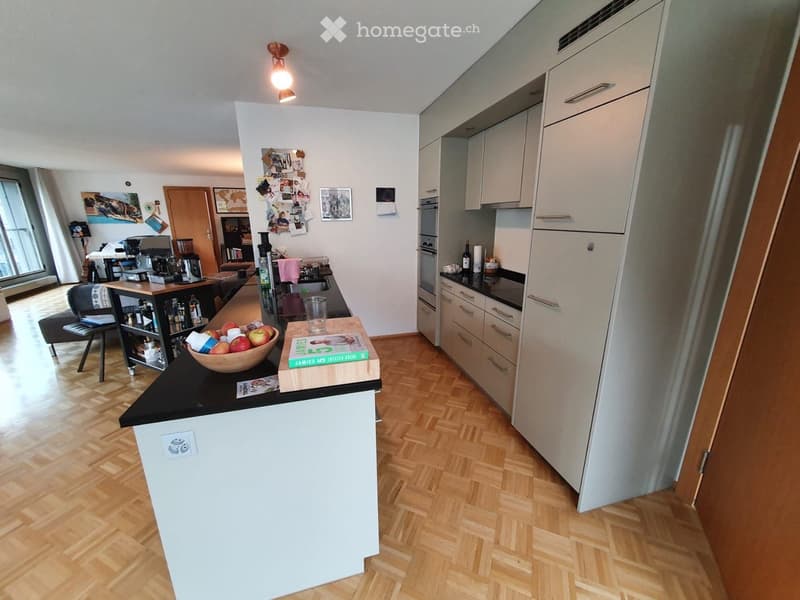 Modern kitchen with white cabinets, black countertops, wooden floor, and a small seating area with a stool and table.