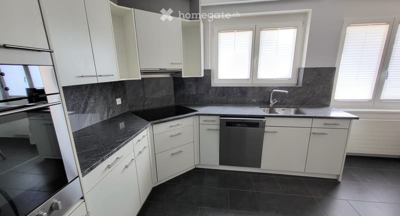 Modern kitchen with white cabinets, dark countertops, and stainless steel appliances, including a sink, faucet, and dishwasher.
