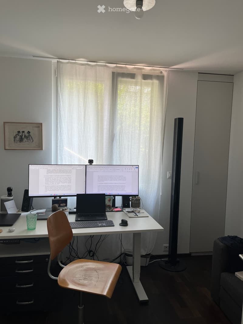 A modern, well-lit workspace with a white desk, a wooden chair, a laptop, dual monitors, and various office supplies.