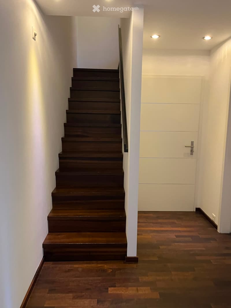 Modern hallway with wooden flooring, white walls, recessed lighting, and a staircase leading upwards.