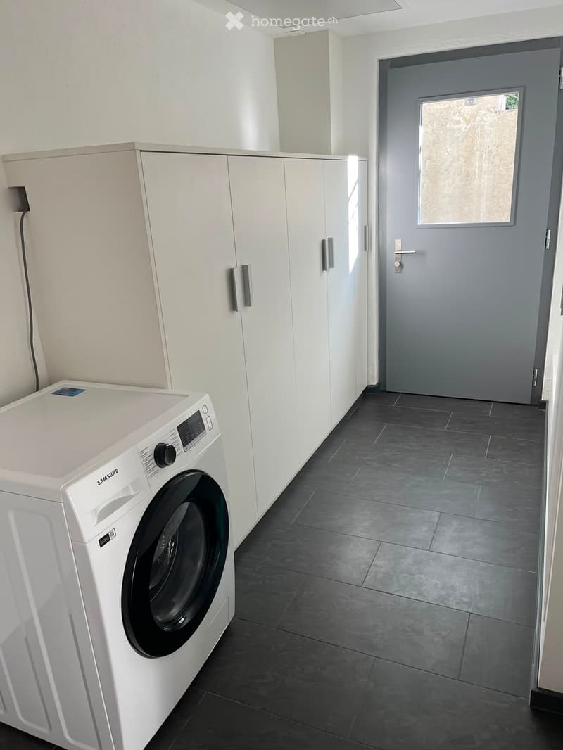 Modern bathroom with a white washing machine, built-in white cabinets, and dark tiled flooring.