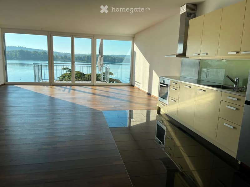 Modern kitchen with light-colored cabinets, stainless steel oven, and a large window offering a scenic lake view.