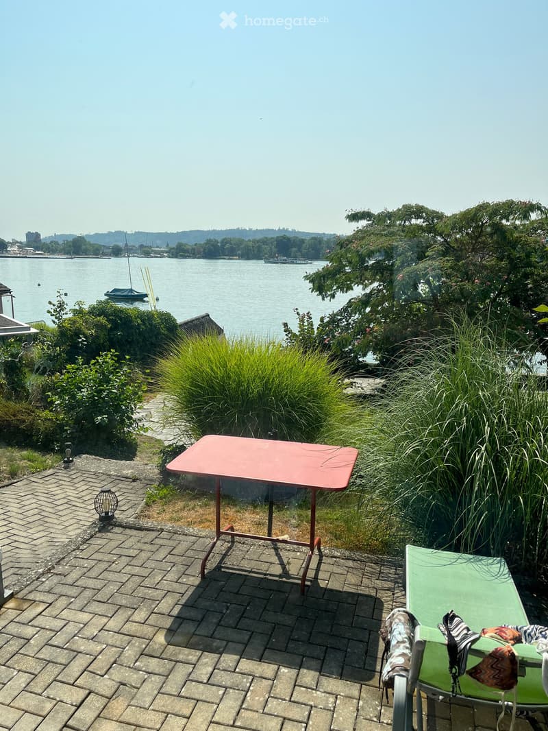 Outdoor patio with a red table, green lounge chair, and scenic water view.