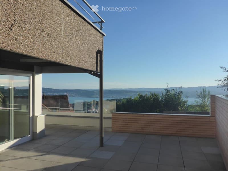 Modern balcony with tiled flooring, wooden railing, and expansive scenic view of a lake and distant mountains.