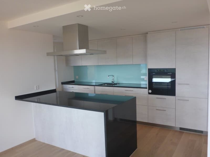 Modern kitchen with white cabinets, black countertops, a central island, and built-in appliances including a range hood and oven.