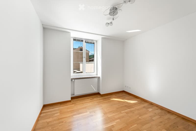 Empty room with wooden flooring, white walls, a window with a view, and a radiator below the window.
