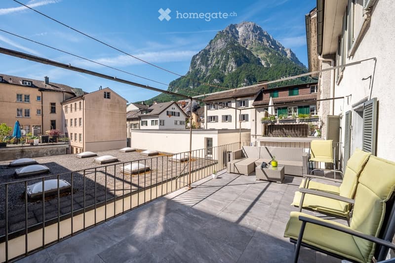 Balcony with a view of a mountain, featuring a sofa, a small table, and a couple of chairs.