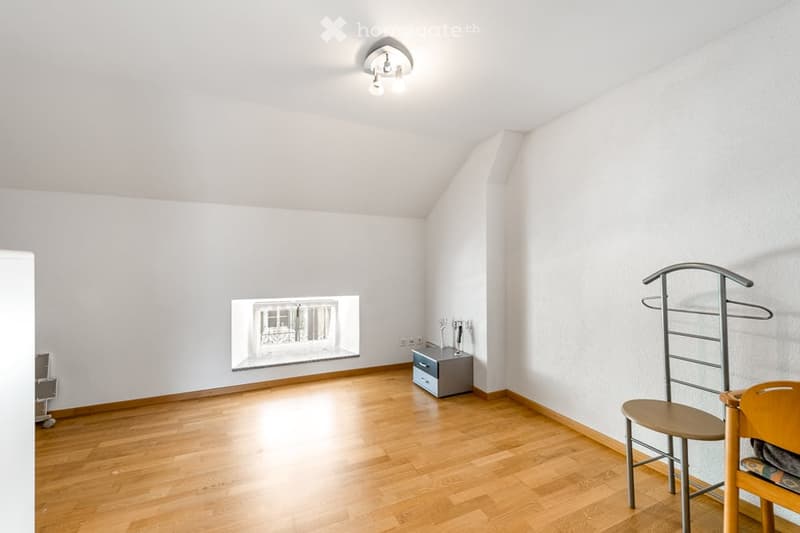Bright, unfurnished room with wooden flooring, white walls, and a skylight window. Contains a single chair, a coat rack, and a small cabinet.