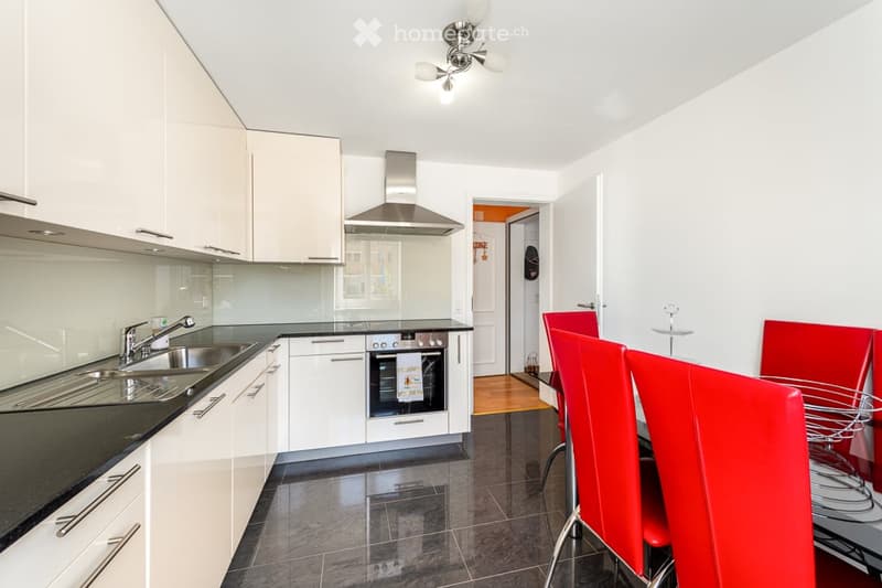 Modern kitchen with white cabinets, stainless steel appliances, and a dining area with red chairs and a glass table.