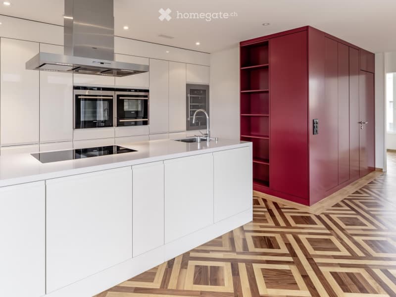 Modern kitchen with white cabinets, stainless steel appliances, a central island, and a red accent wall.