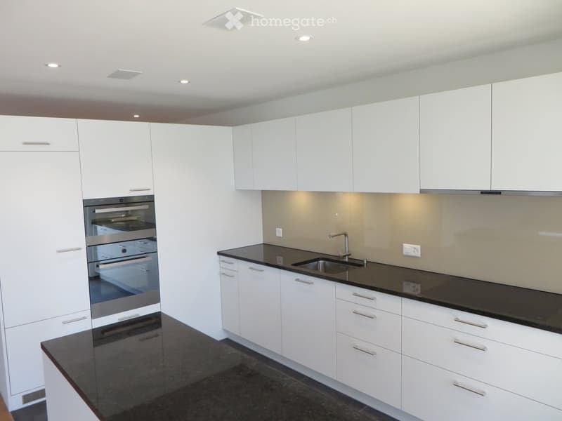Modern kitchen with white cabinets, black countertops, and stainless steel appliances including an oven and sink.