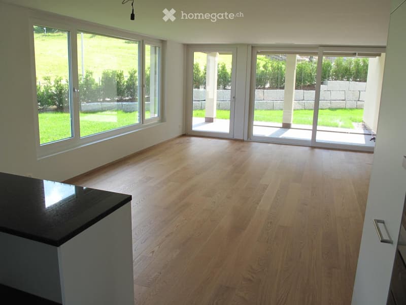 Empty room with wooden flooring, large windows, and sliding glass doors leading to a patio.