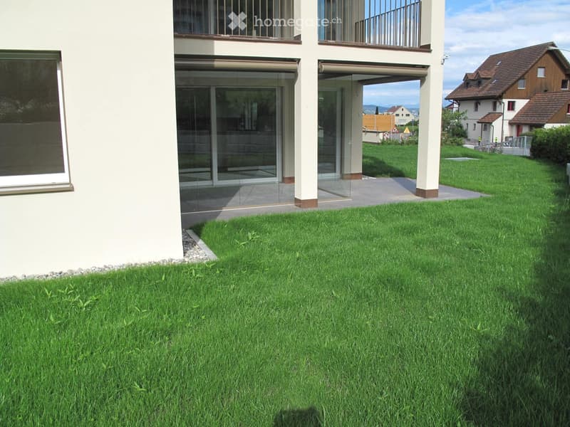 Well-maintained lawn in front of a modern house with large glass doors and a balcony.