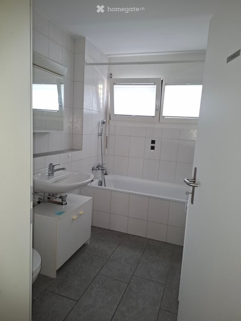 Modern bathroom with white tiles, a sink, bathtub, mirror, and cabinet.