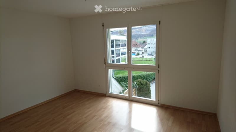 Empty room with wooden flooring and large windows offering a view of the outside area.