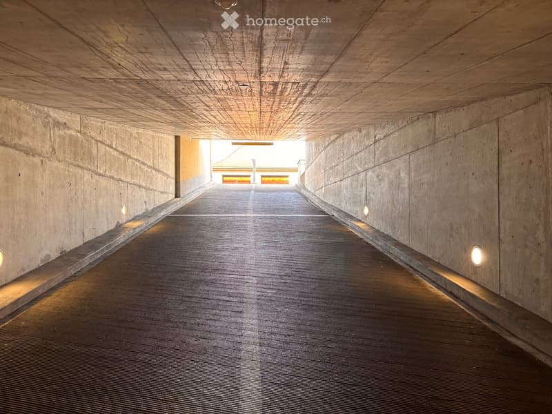 Modern concrete corridor with sleek, polished floor and embedded lighting, leading to an open doorway at the end.