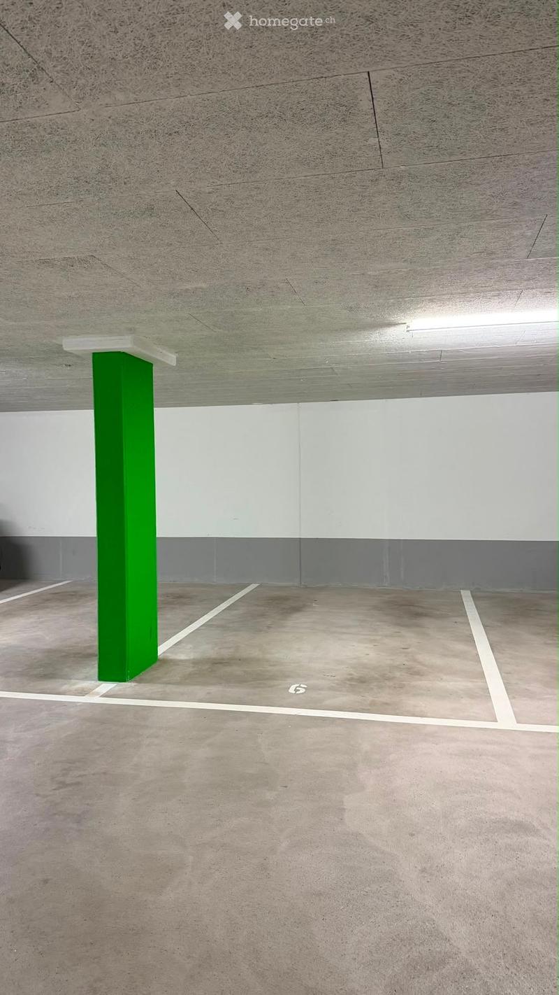 Empty parking space with concrete floor, white painted lines, and a green support pillar.