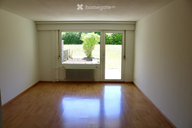 Empty room with wooden flooring, white walls, large window and sliding glass door leading to an outdoor area.