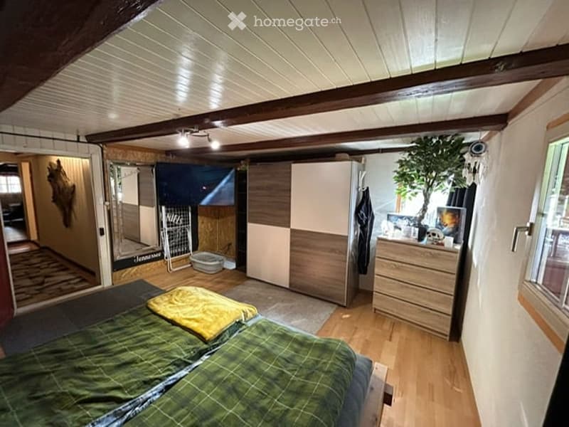 Cozy bedroom with wooden flooring, slanted ceiling, bed with green and yellow blankets, wardrobe, dresser, mirror, and a small plant on the dresser.