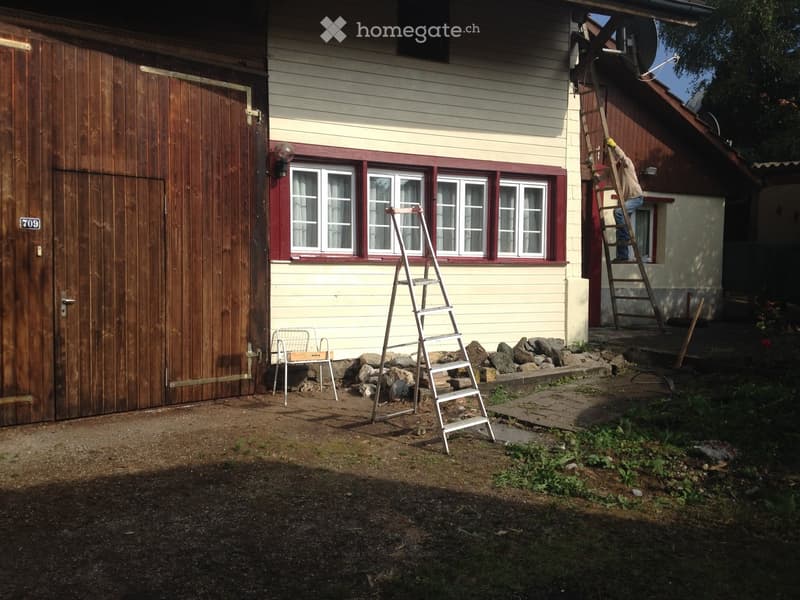 A residential outdoor area with a house, garage, ladders, and a small table with a chair.