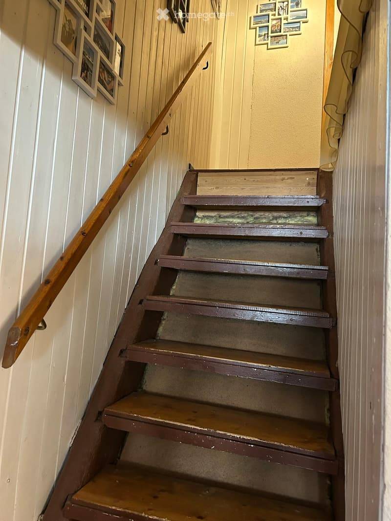 Wooden staircase with a handrail, featuring a mix of dark and light wooden steps, and framed pictures on the walls.