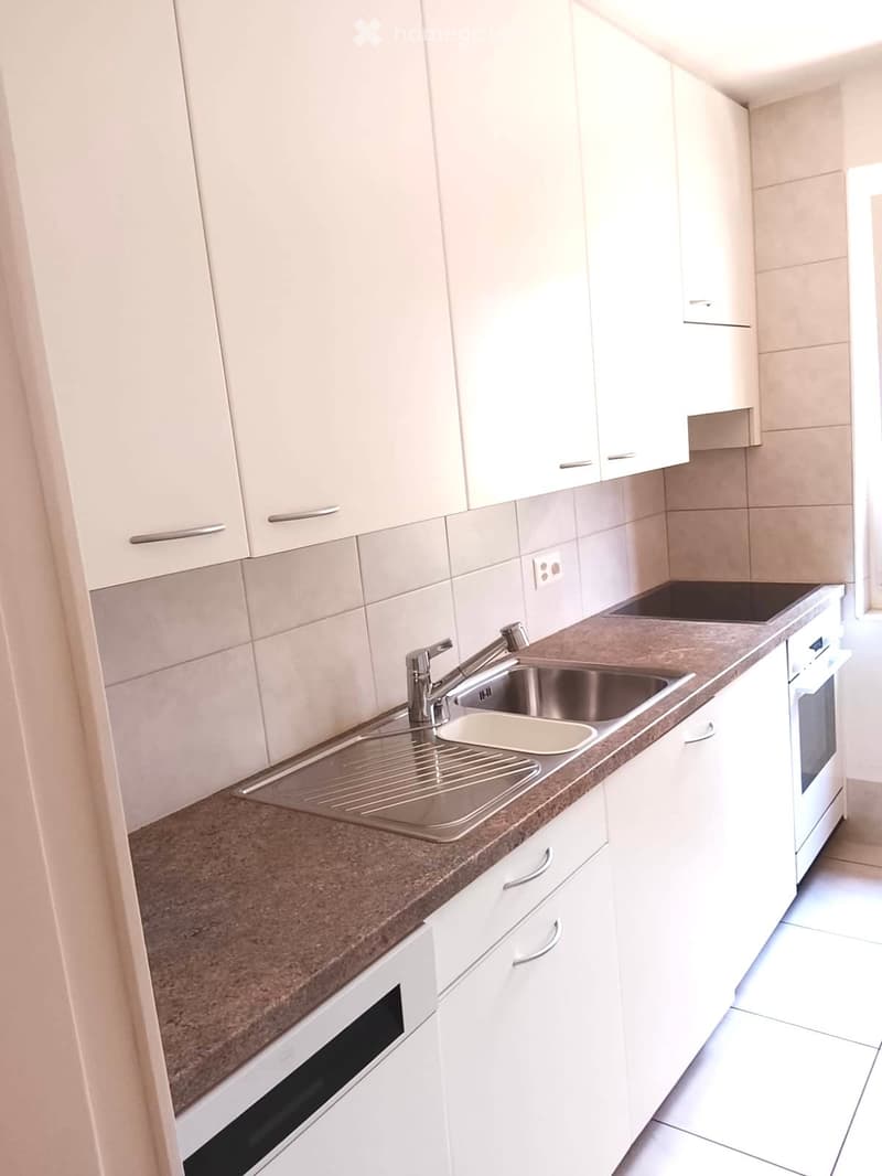 Modern kitchen with white cabinets, a stainless steel sink, and built-in oven. Countertop is brown with a tiled backsplash.