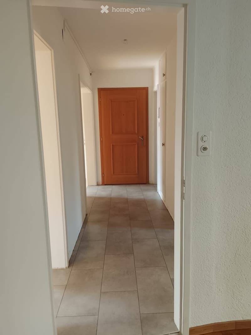 Empty hallway with tiled floor, white walls, and a wooden door at the end.
