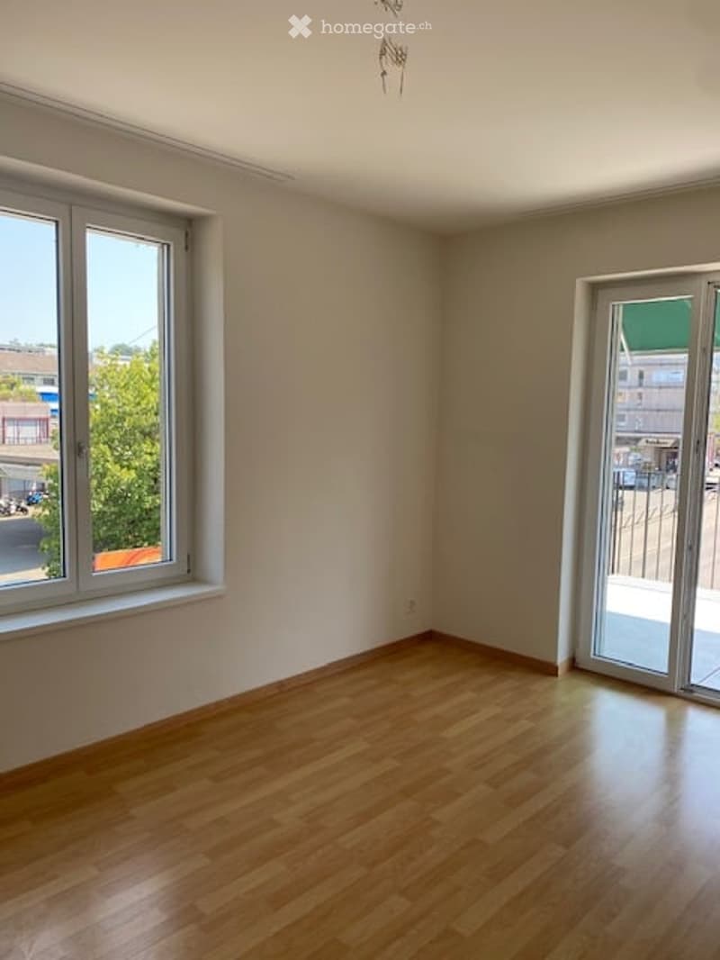 Empty room with wooden flooring, large windows, and a sliding glass door leading to a balcony.