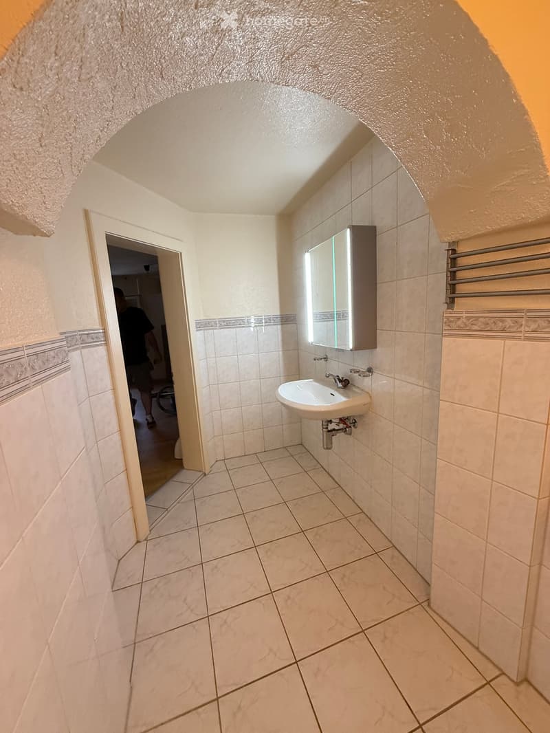 Small bathroom with white tiled walls and floor, a sink with a mirror cabinet, and a radiator on the right side.