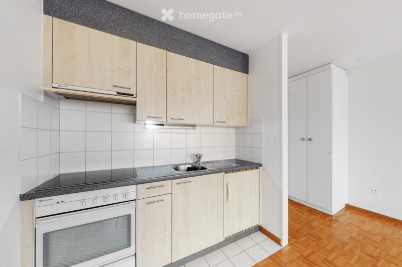Modern kitchen with light wood cabinets, white tiled backsplash, and a stainless steel sink. Features an oven, countertop, and built-in cabinets.