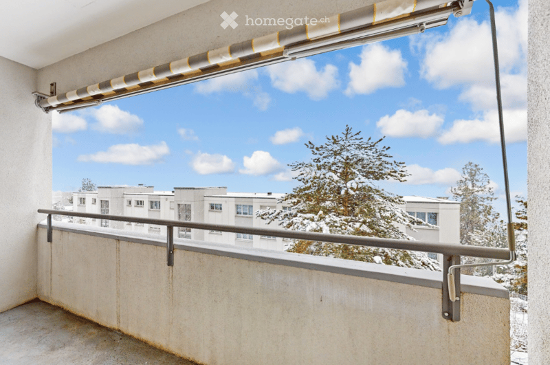 Balcony with a view of a snowy landscape, featuring a retractable awning and metal railing.